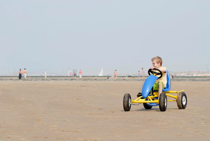 young boy in blue & yellow go-cart on the  beach 