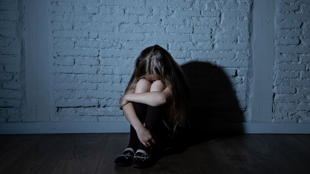 Sad desperate young girl suffering from bulling and harassment felling lonely, unhappy desperate and hopeless sitting against the wall, dark light. School isolation, abuse and bullying concept (Sad desperate young girl suffering from bulling and haras