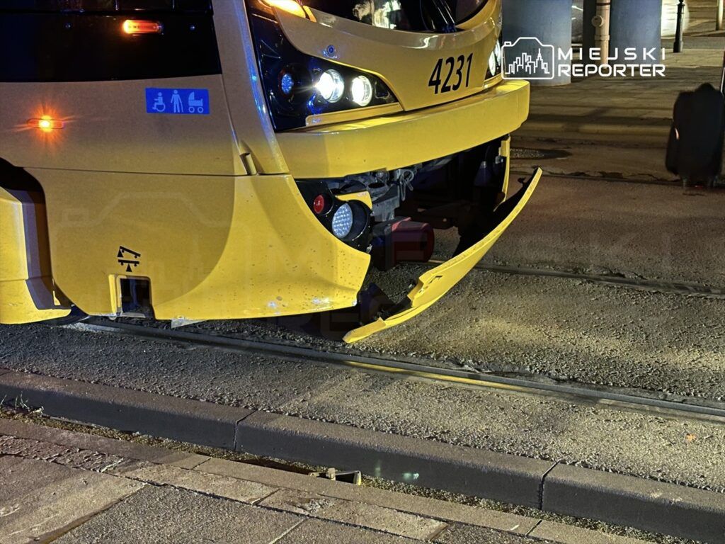 Uszkodzony tramwaj z odłamanym przodem stoi na torach, w otoczeniu oświetlonych ulic.