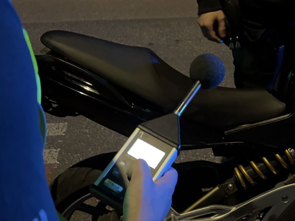 Osoba trzymająca miernik hałasu z mikrofonem blisko siedzenia motocykla na ulicy w nocy.