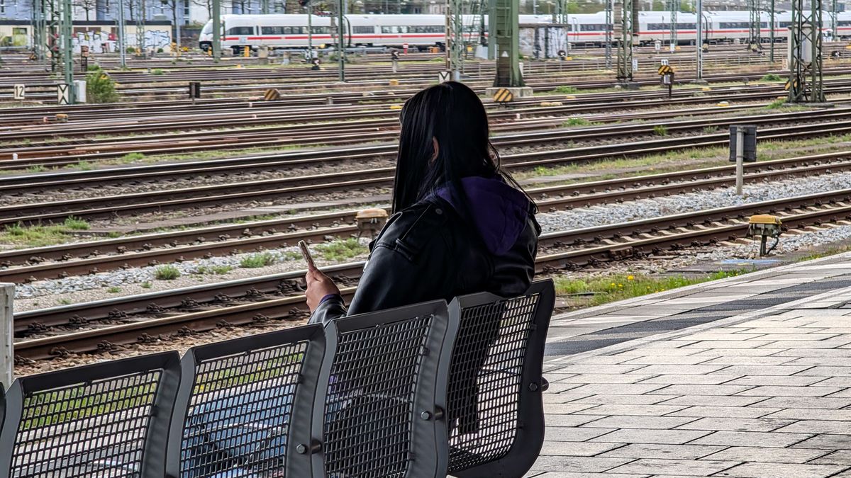 A woman sits on a bench looking at her phone while waiting for a train at Hackerbrucke station near multiple railway tracks in Munich, Upper Bavaria, Bavaria, Germany, on April 13, 2025. (Photo by Michael Nguyen/NurPhoto via Getty Images)