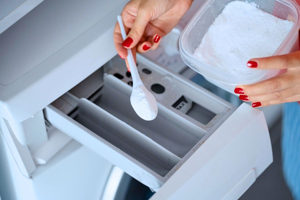 The woman pours detergent into the washing machine.