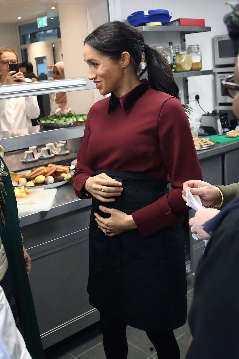 LONDON, ENGLAND - NOVEMBER 21: Meghan, Duchess of Sussex cradles her bump as she visits the Hubb Community Kitchen to see how funds raised by the 'Together: Our Community' Cookbook are making a difference at Al Manaar, North Kensington on November 21, 2018 in London, England.