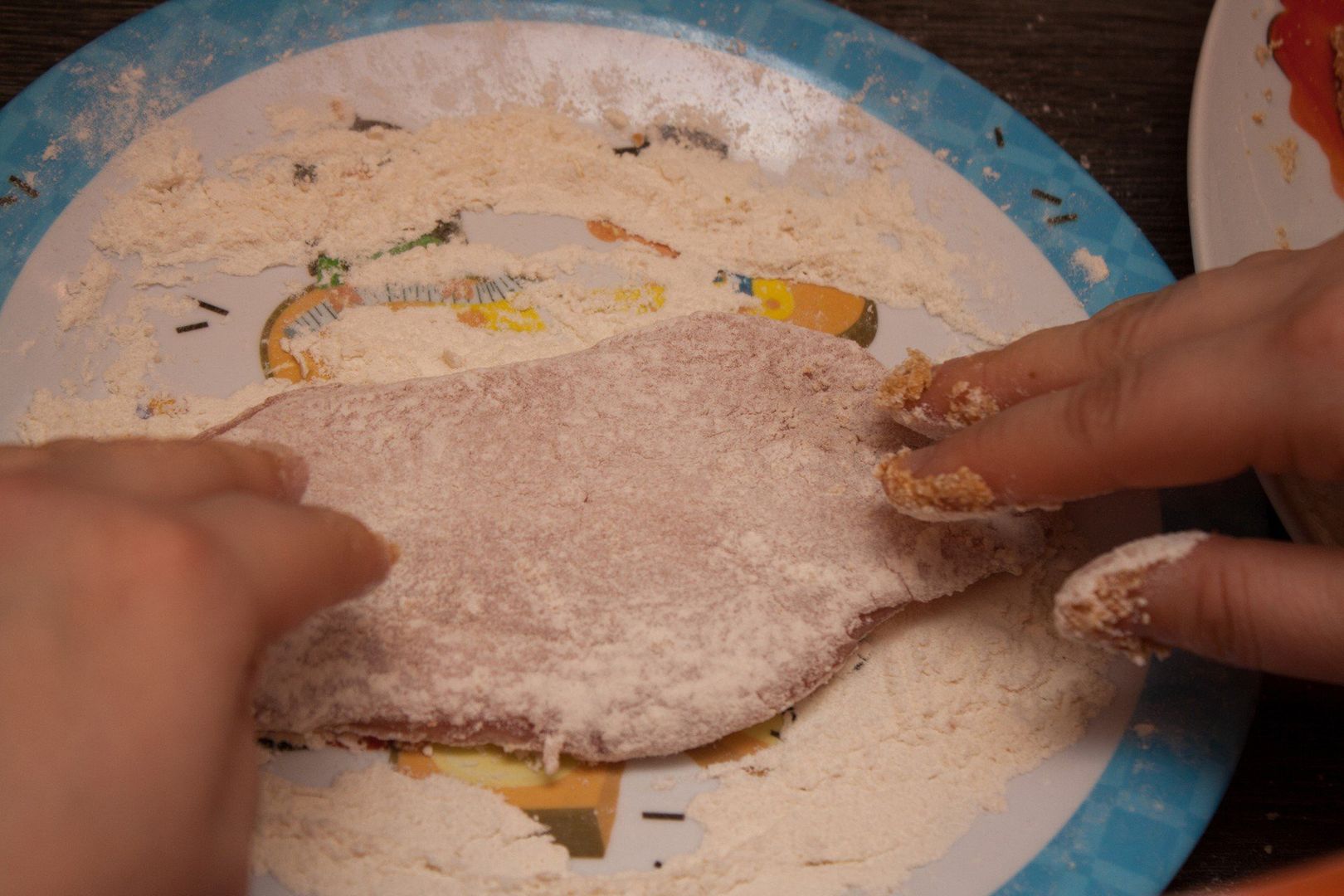 Two hands putting flour on meat making a wiener schnitzel