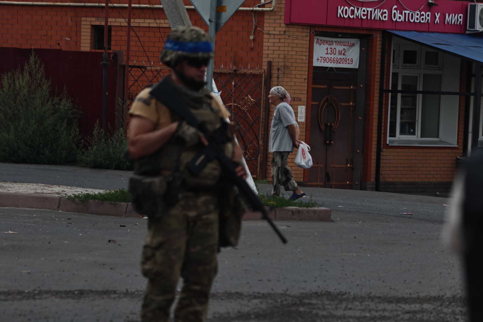 SUDZHA, RUSSIA - AUGUST 16: A Ukrainian military member holds a weapon, and a woman walks a street on August 16, 2024 in Sudzha, Russia. The fighting in the Kursk Oblast began on August 6, 2024, when the Armed Forces of Ukraine crossed the Russian-Ukrainian border near the city of Sudzha and began to advance deep into Russian territory, and in a few days took control of dozens of settlements in Kursk region. (Photo by Yan Dobronosov/Global Images Ukraine via Getty Images)