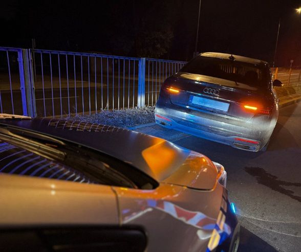 Policyjny radiowóz z włączonymi sygnalizatorami zatrzymuje czarne auto na drodze nocą.