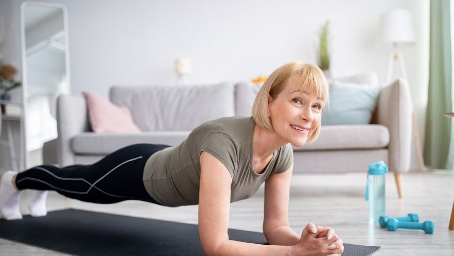 Home training concept. Smiling senior woman doing elbow plank on yoga mat in living room