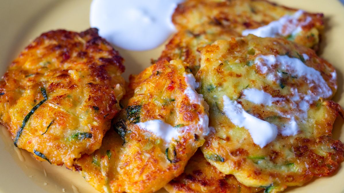 Close-up of pancakes with zucchini and vegetables laid out on a plate and served with sour cream. Top view, flat layClose-up of pancakes with zucchini and vegetables laid out on a plate and served with sour cream. Top view, flat layDarkwisper