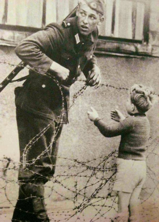Niemiecki żołnierz pomagający chłopcy przejść przez blokadę przy Murze Berlińskim (1961)