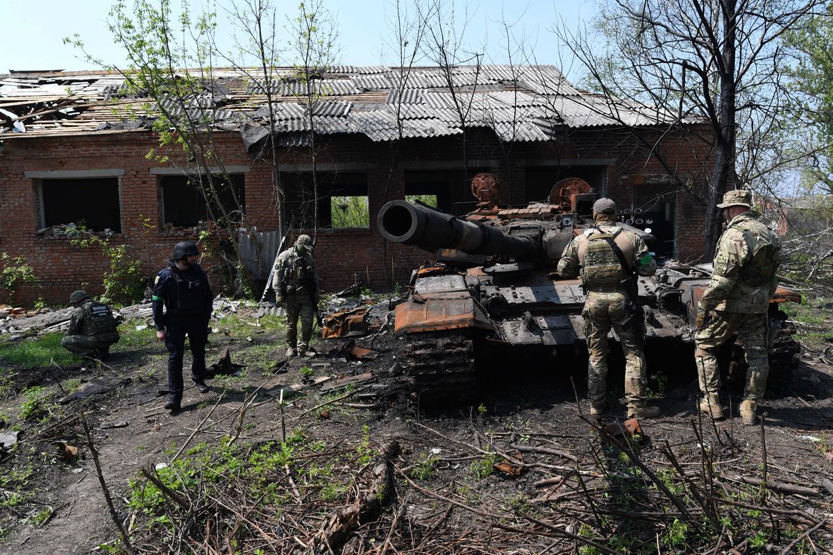 Wojskowi śledczy i ukraińscy żołnierze obserwują zniszczony rosyjski czołg 