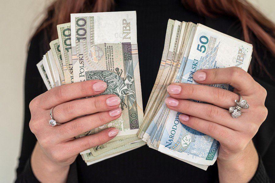 of several banknotes of 100 zlotys of Polish money held in the hands of a woman in a suit.