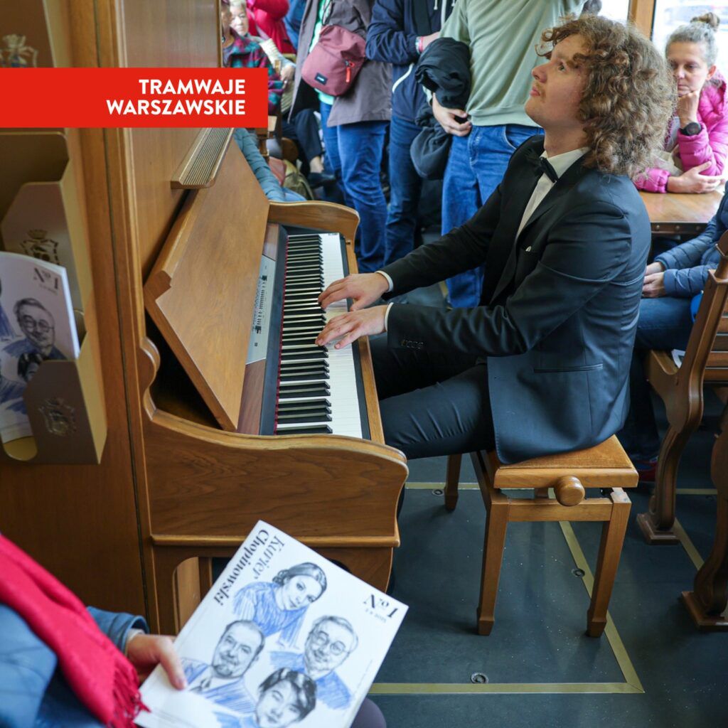 Mężczyzna w garniturze gra na pianinie w tramwaju, a pasażerowie słuchają i obserwują.