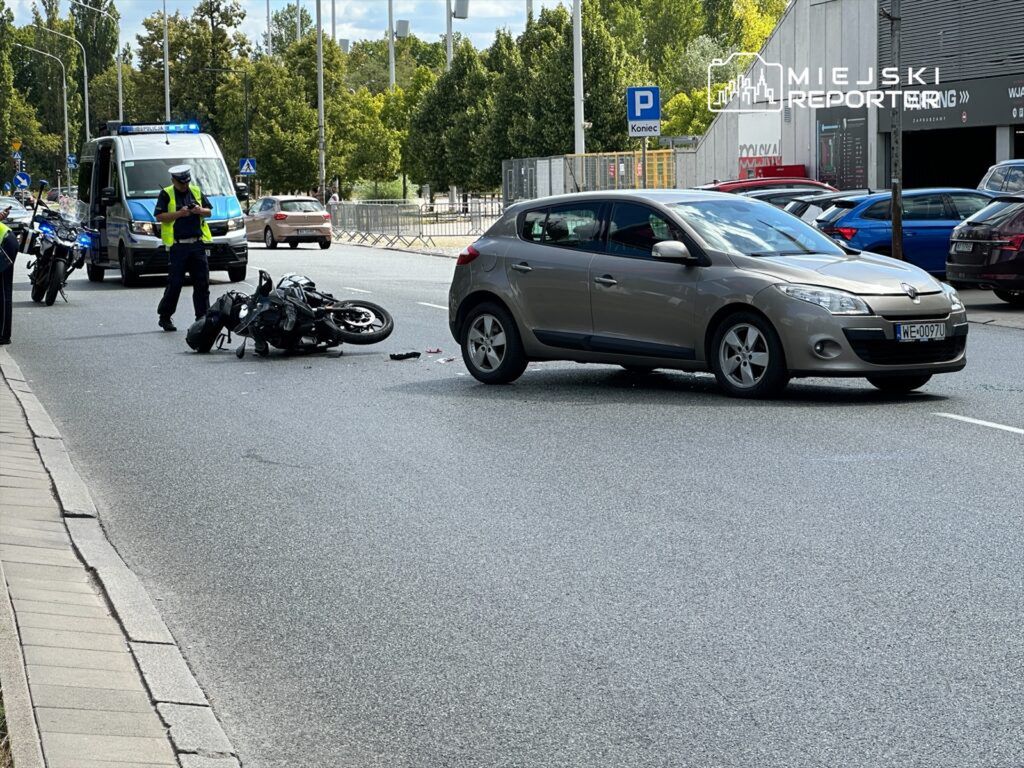 Motocykl leży na jezdni, obok stoi policyjny radiowóz, a funkcjonariusz zbiera informacje.
