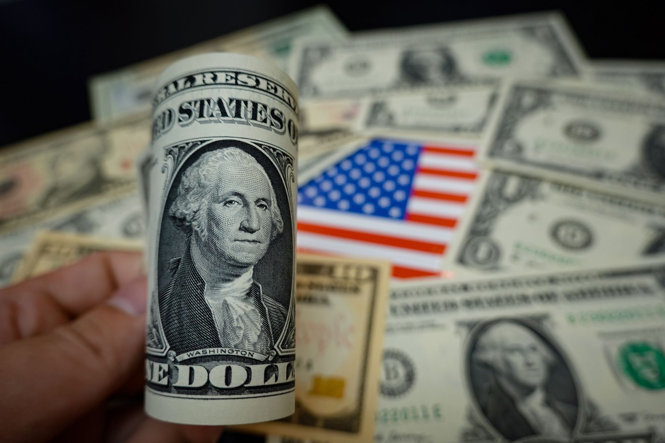 CHINA - 2024/09/19: In this photo illustration, some dollar banknotes are displayed on a table, along with an American flag. (Photo Illustration by Sheldon Cooper/SOPA Images/LightRocket via Getty Images)