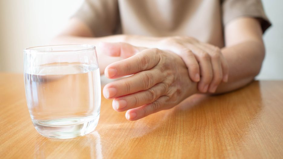 Elderly woman hands w/ tremor symptom reaching out for a glass of water on wood table. Cause of hands shaking include Parkinson's disease, stroke or brain injury. Mental health neurological disorder.
age,middle east,female,neuropathy,nerve,paralysis,numbness,patie