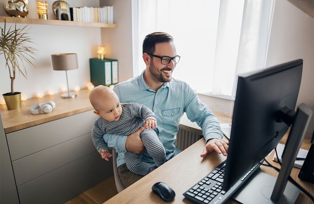 Un homme avec un nouveau-né devant un ordinateur sécurise un appartement en ligne