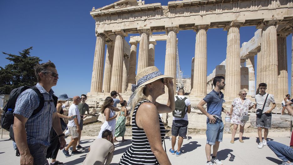 A woman holds her hat in front of the Parthenon because of the strong wind. Crowds of tourists and local visitors in front of the Parthenon, an ancient temple dedicated to the goddess Athena, on the Akropolis of Athens on the known sacred rock. People are seen walking and takings pictures of the ancient monument, while wearing hats because of the Greek sun. The Acropolis of Athens is an ancient citadel located on a rocky outcrop above the city of Athens and contains the remains of several ancient buildings of great architectural and historical significance, the most famous being the Parthenon attracting millions of tourists and visitors every year. It was built in 432BC by the architects Iktinos and Calicrates with famous sculptures from Phidias inside. Acropolis is a UNESCO World Heritage Site. Greece is facing an increased wave of tourist arrivals in pre pandemic levels, as of summer 2022 the numbers are exceeding the era before the COVID-19 Coronavirus travel restriction measures. Tourism is one of the main income sources of the country. Athens, Greece on July 2022 (Photo by Nicolas Economou/NurPhoto via Getty Images)