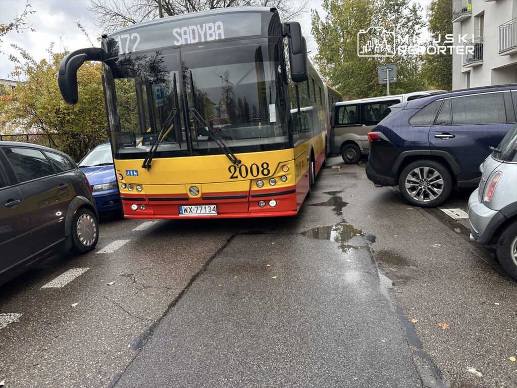 Autobus linii 172 utknął między zaparkowanymi samochodami na wąskiej ulicy, otoczony przez pojazdy.