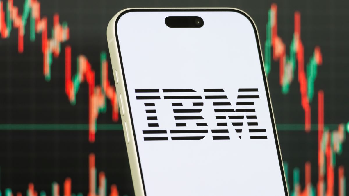 CHONGQING, CHINA - JANUARY 22: In this photo illustration, a smartphone displays the logo of International Business Machines Corporation (NYSE: IBM), the U.S.-based technology company known for its enterprise software, cloud computing and artificial intelligence services, in front of a screen showing the company's stock market chart on January 22, 2026, in Chongqing, China. (Photo illustration by Cheng Xin/Getty Images)
