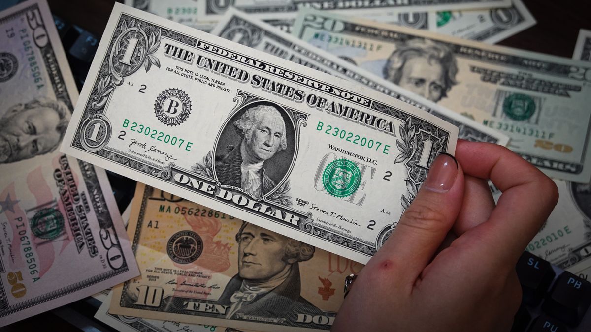 SHANGHAI, CHINA - 2024/08/31: In this illustration, a person is holding some US dollar cash bills in his hands, some of which are placed on a table. (Photo Illustration by Sheldon Cooper/SOPA Images/LightRocket via Getty Images)