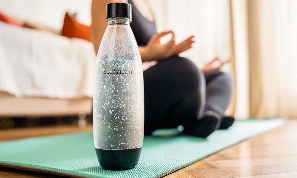 Kobieta medytująca na macie w domu i butelka wodą gazowaną SodaStream 
