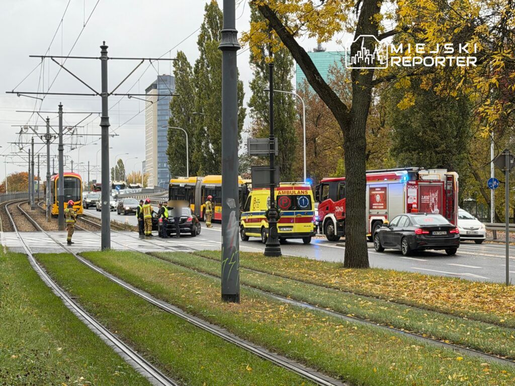 Kilku ratowników i policjantów zabezpiecza miejsce wypadku drogowego obok torów tramwajowych, w tle pojazdy służb ratunkowych.