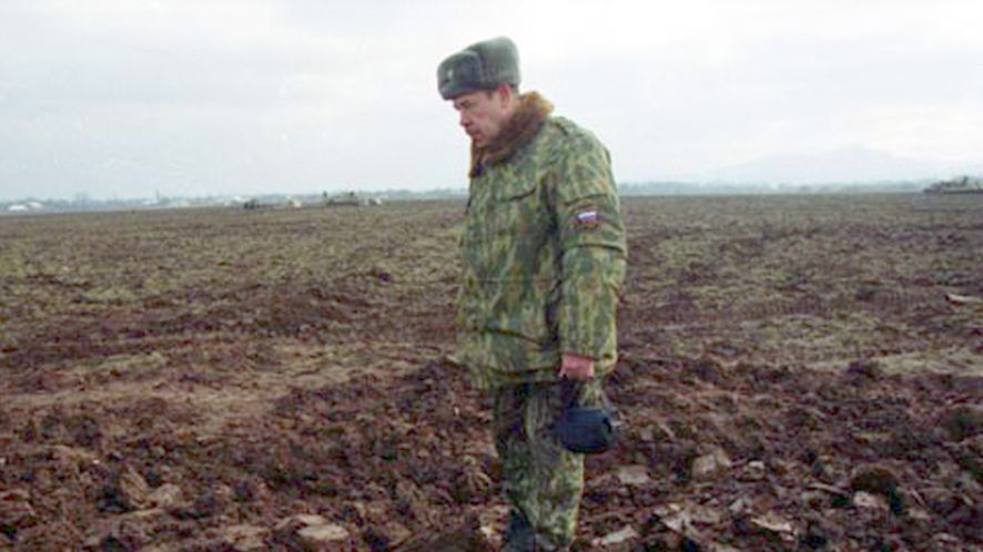 Rosyjski żołnierz stoi na masowym grobie Czeczenów. Spod ziemi wystają ich twarze. 2000 r.
