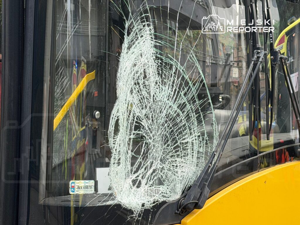 Zniszczona szyba frontowa autobusu z pęknięciami, znajdującego się na miejskiej ulicy.