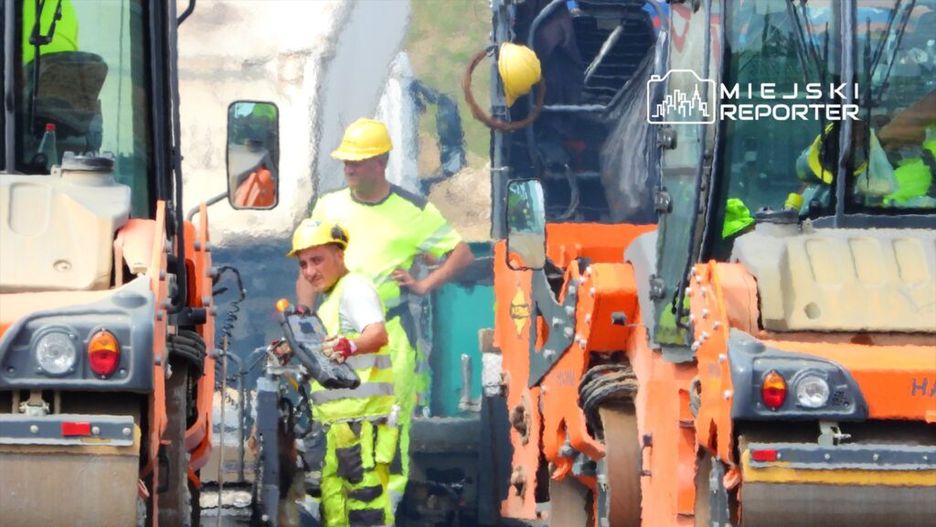 Mężczyzna w żółtej kamizelce i kasku obsługujący maszynę budowlaną na placu robót drogowych.