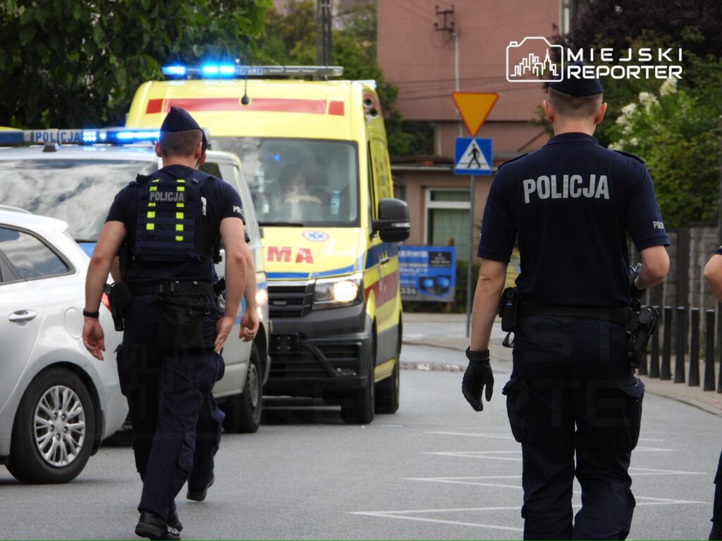 Dwóch policjantów w mundurach idzie w stronę karetki pogotowia na miejskiej ulicy.