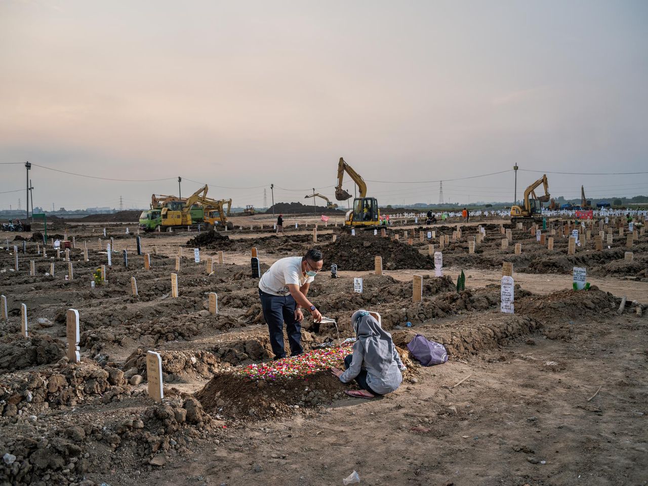 21.07.2021 r., Północna Dżakarta, Indonezja. Krewni zmarłej na COVID-19 przyozdabiają grób płatkami róż i polewają je wodą. W lipcu 2021 roku, w samej Dżakarcie średnia zakażeń wyniosła 50 000 przypadków.