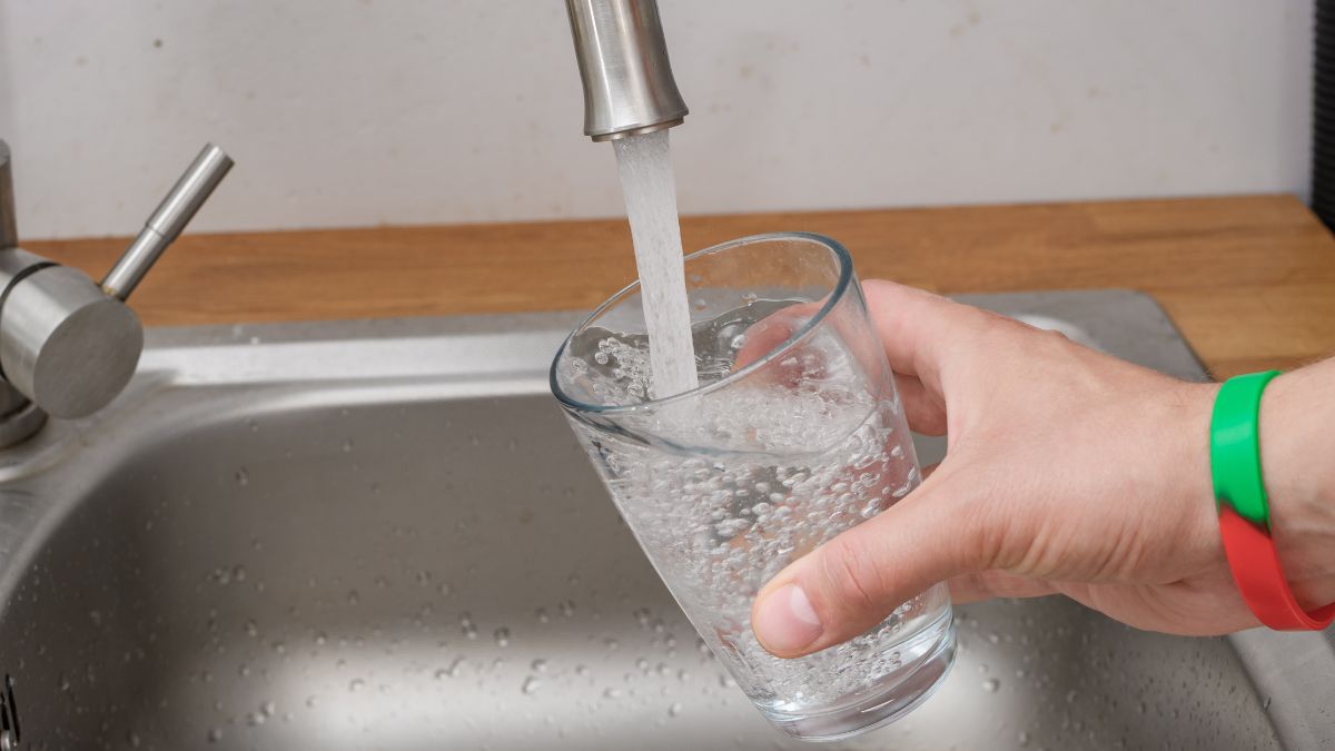Człowiek nalewa wodę z kranu do szklanki. 