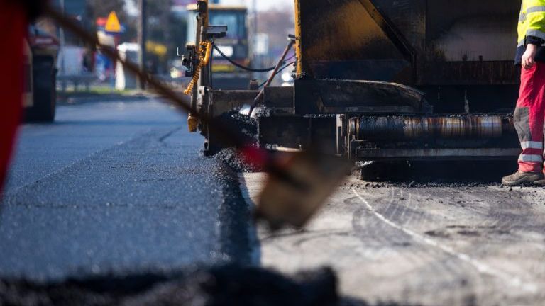 Robotnicy układają nową nawierzchnię asfaltową na drodze, obok pracuje maszyna do asfaltu.