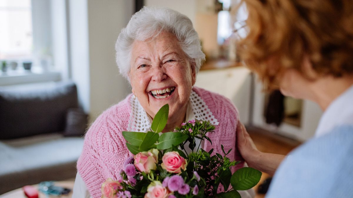 Uśmiechnięta starsza pani przyjmuje kwiaty i życzenia