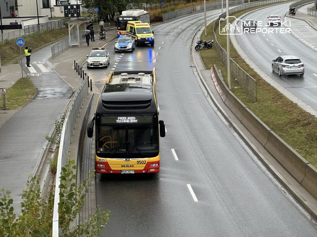 Autobus przystankowy zatrzymany na jezdni, obok widać radiowozy policyjne oraz ambulans, na chodniku przechodnie.
