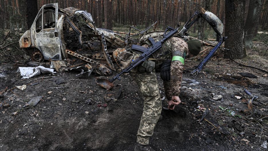 KYIV, UKRAINE - APRIL 14: A Ukrainian soldier clears the remnants of a burnt vehicle on the road of the Moshun village in the Kyiv province, Ukraine on April 14, 2022. Ukrainian civilians trying to return to their homes are not allowed in due to the ongoing mine clearance activities in some villages that the Ukrainian army regained control of as Russian attacks continue all over the country. (Photo by Metin Aktas/Anadolu Agency via Getty Images)