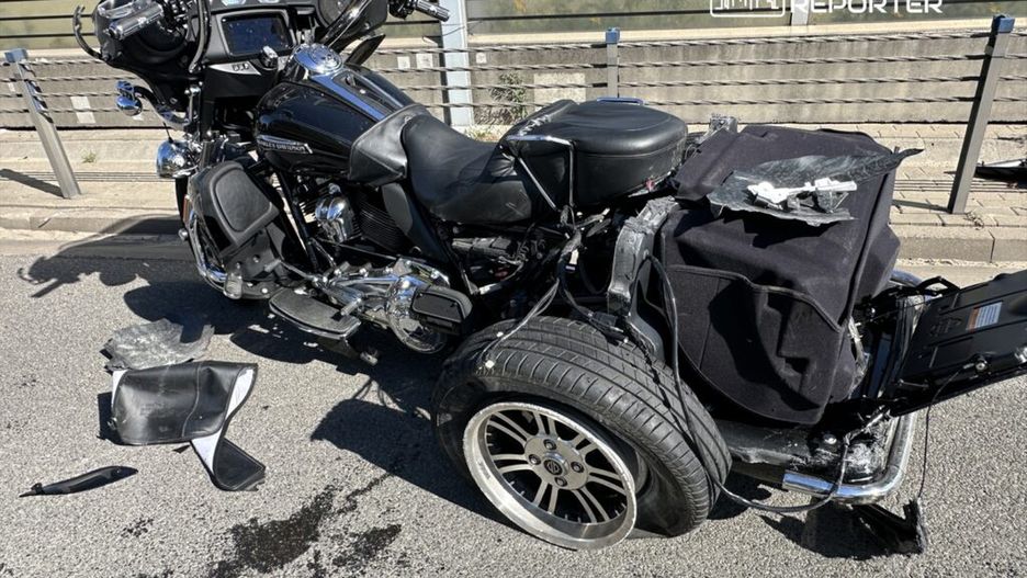 Uszkodzony motocykl typu trójkołowego leży na asfalcie, obok widoczne fragmenty zniszczonych elementów i plama oleju.
