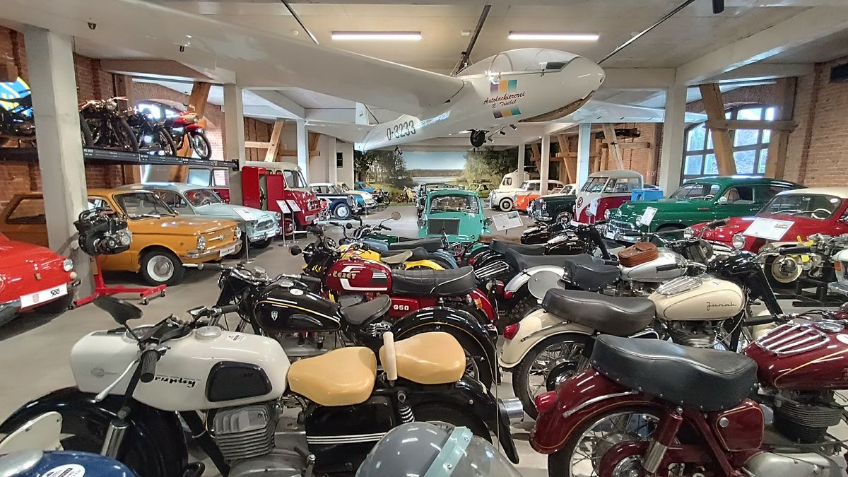 Sala Muzeum Motoryzacji i Techniki Zamek Topacz: motocykle na pierwszym planie, zabytkowe samochody i biały szybowiec pod sufitem