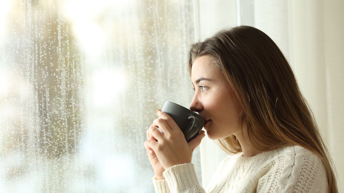 Kobieta z kubkiem patrząca na padający deszcz