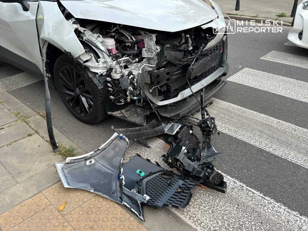 Uszkodzony samochód osobowy z zerwaną przednią częścią oraz częściami leżącymi na jezdni.