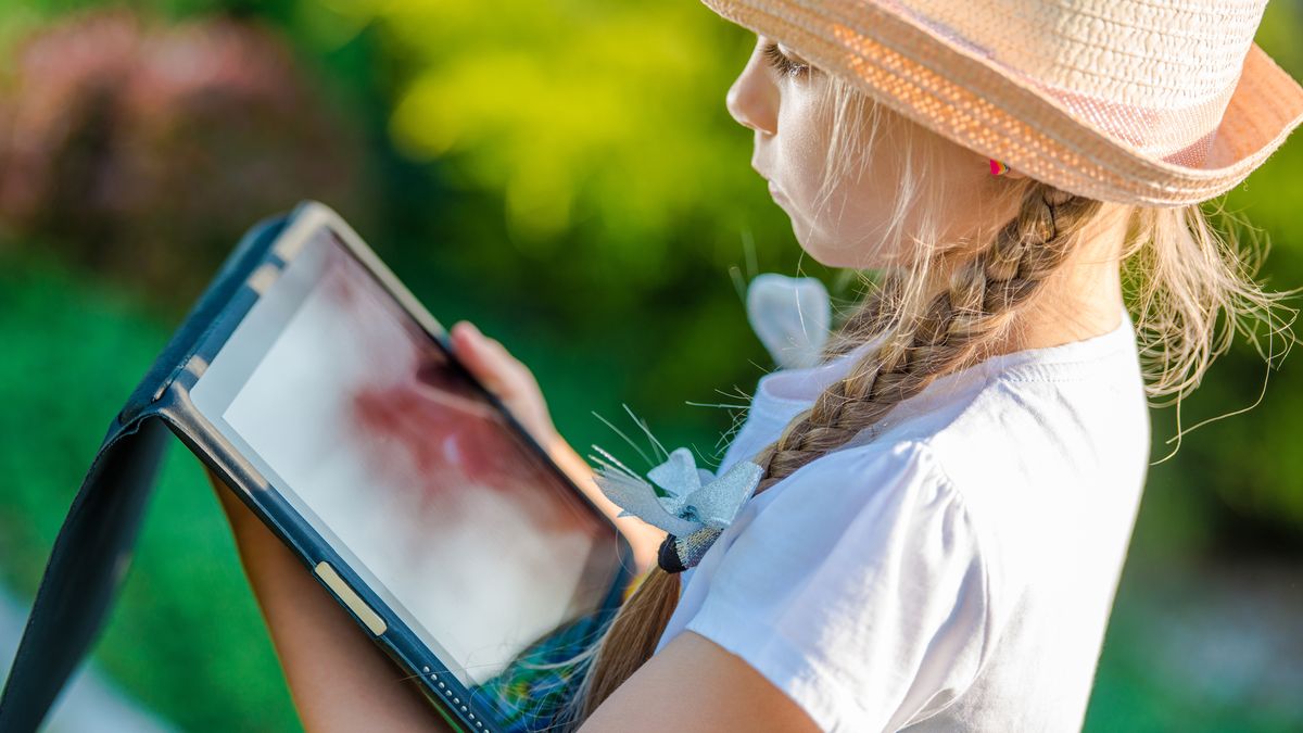 Young Caucasian Girl Playing with Tablet Device in the Garden. Closeup Photo