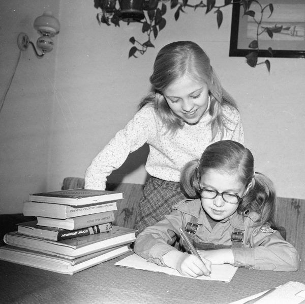 Dziewczynka odrabia lekcje. Widoczna sterta książek – m.in. Piotr Bąk – "Gramatyka języka Polskiego", "Popularny atlas świata", "Słownik geograficzny" 