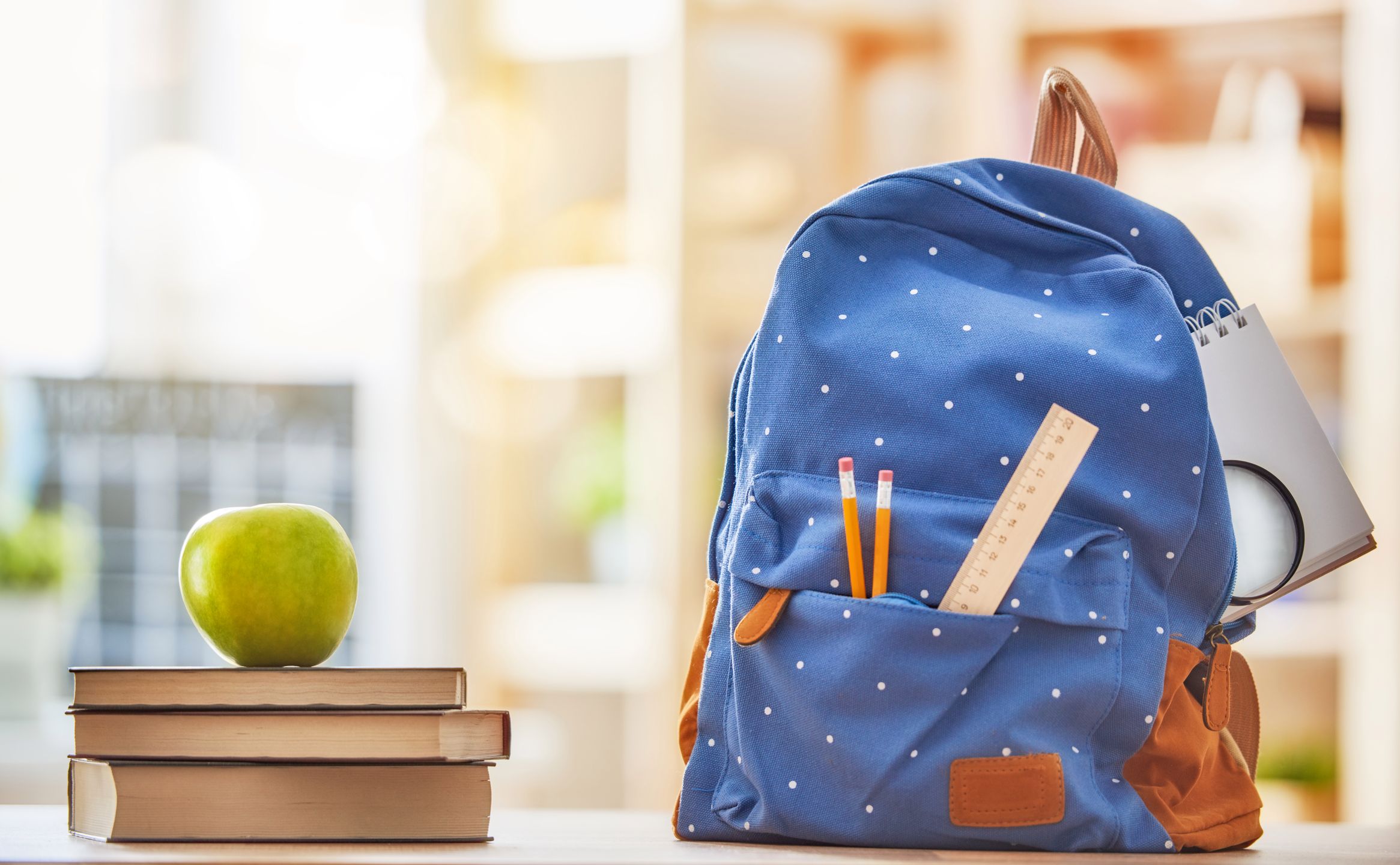 Back to school and happy time! Apple, pile of books and backpack on the desk at the elementary school. 