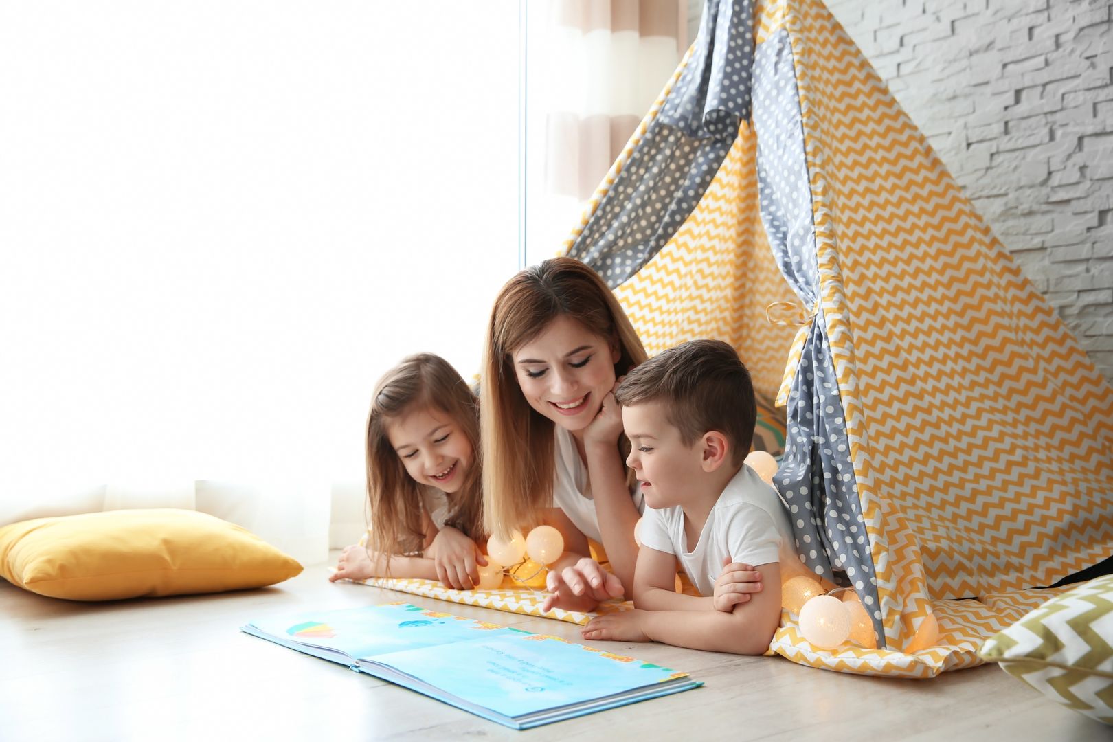 Nanny and little children reading book in tent at home