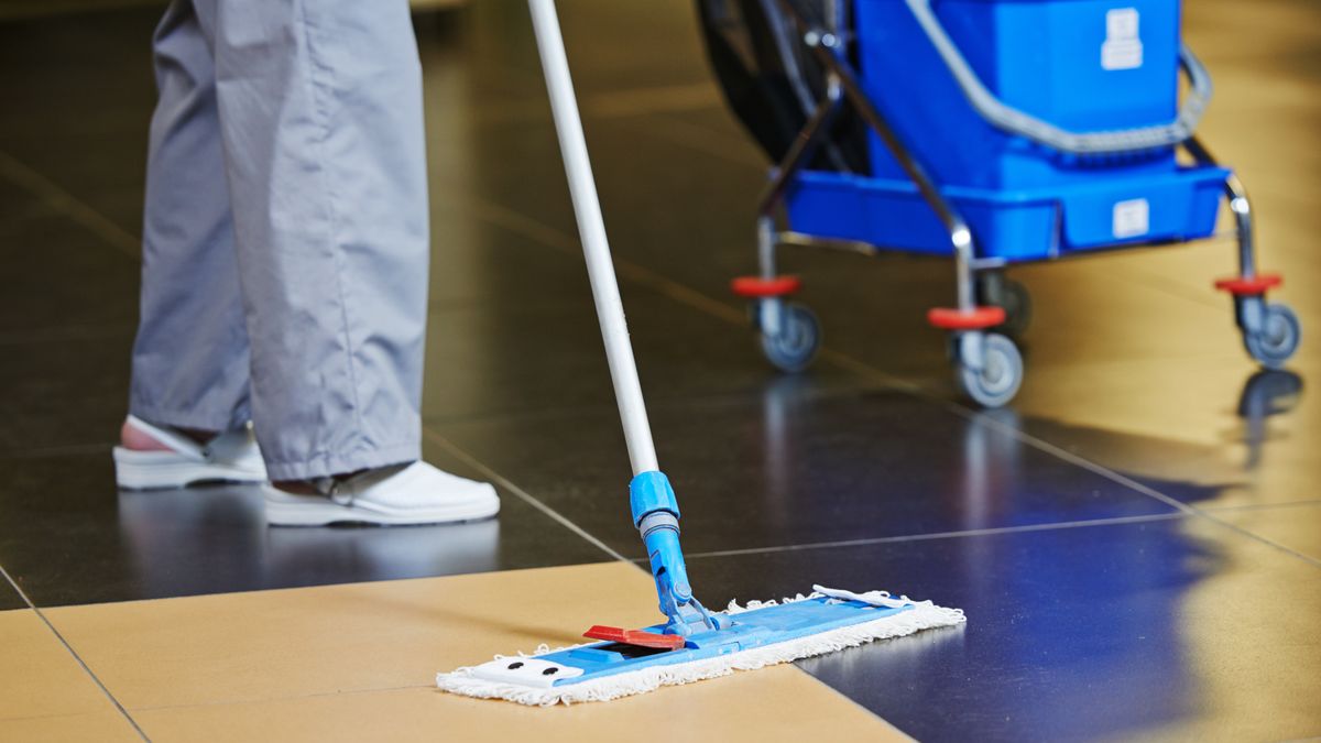 cleaner with mop and uniform cleaning hall floor of public business building
