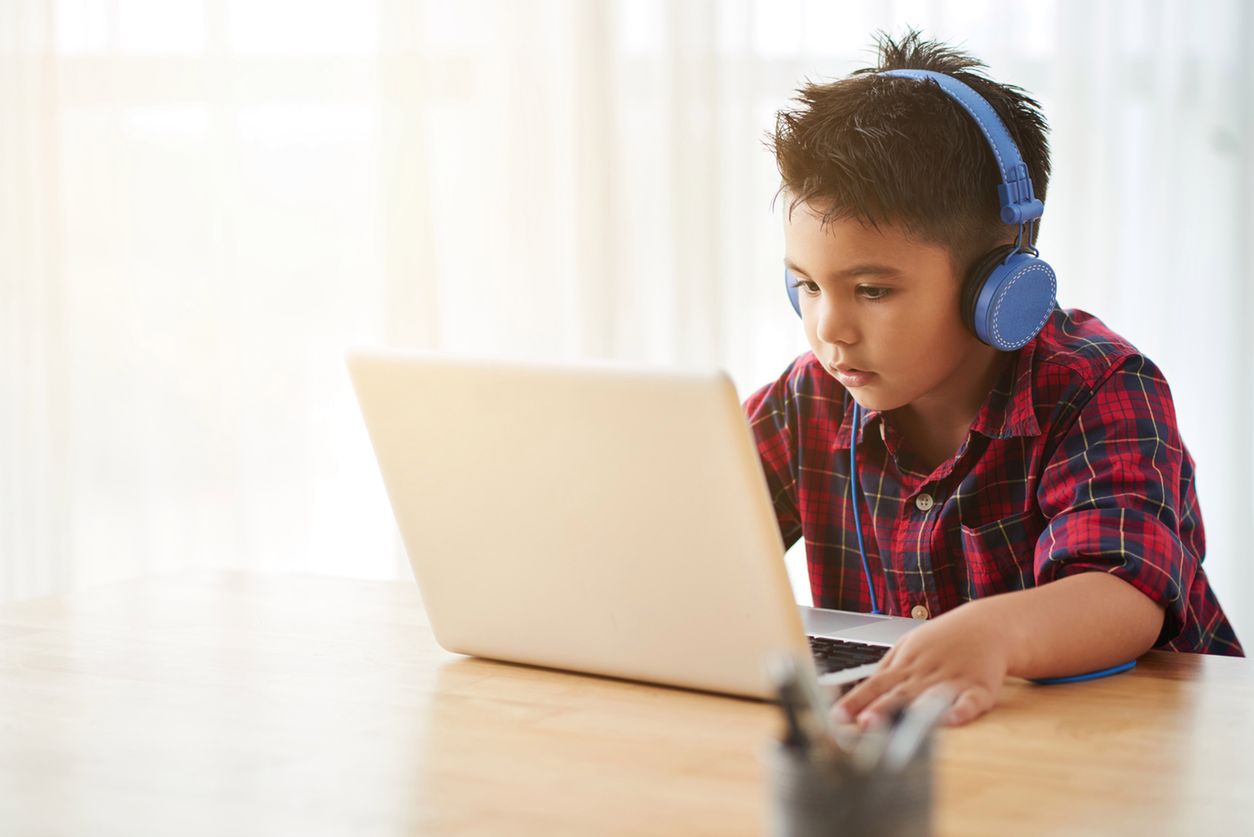 Cute little boy in headphones watching something on laptop at home 