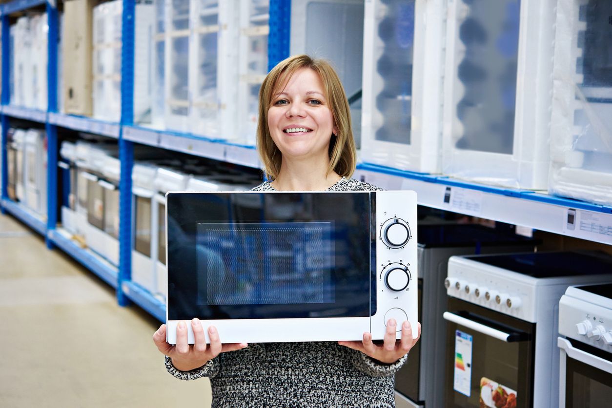 Happy woman shopper buys a microwave in the store 