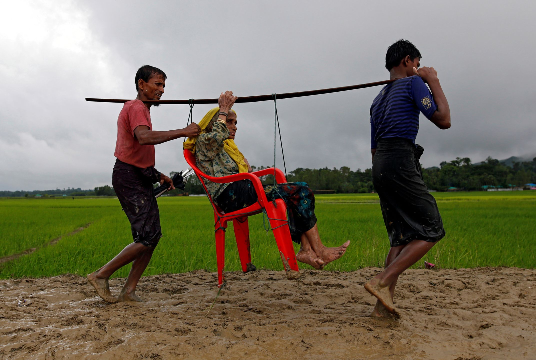 Młodzi uchodźcy niosą kobietę przez granicę między Mjanmą i Bangladeszem