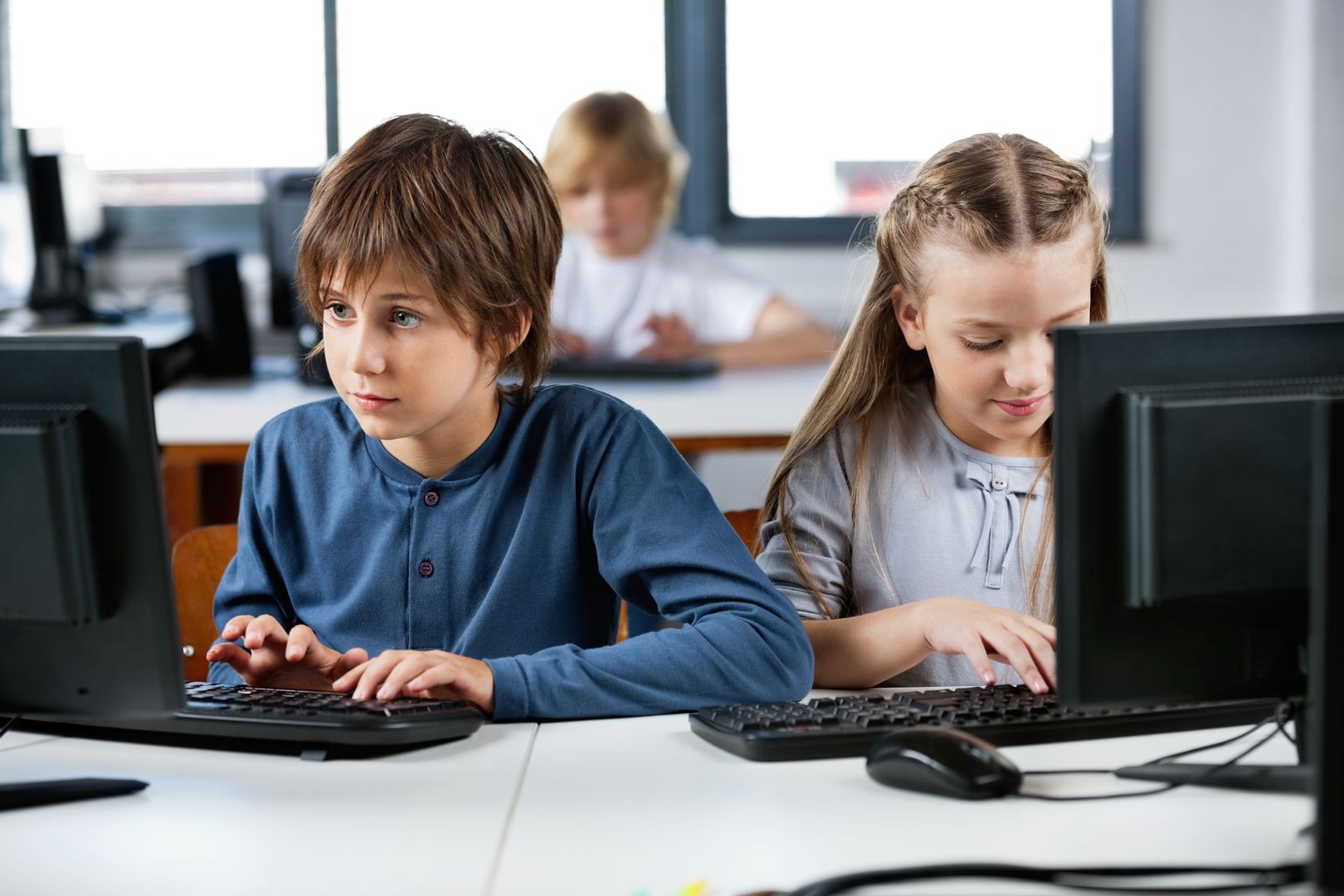 Cute little schoolchildren using desktop PC at desk in computer lab