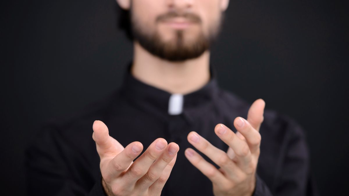 Praying priest. Portrait of priest standing isolated on black